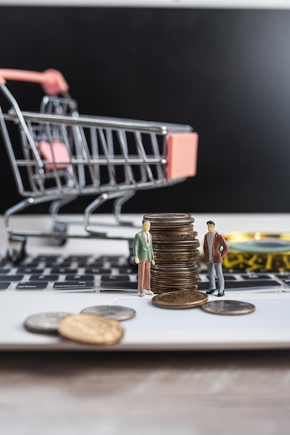 Miniaturmenschen mit uns Münze und Einkaufswagen auf Laptop für E-Commerce-Einkauf Einsparung von Investitionen oder Kaufkonzept