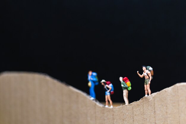 Miniaturmenschen: Reisender mit dem Rucksack, der auf den Papierberg geht