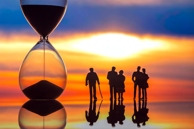 Foto miniaturmenschen-silhouetten verschiedener menschen, die den sonnenuntergang neben dem ende der sanduhr beobachten