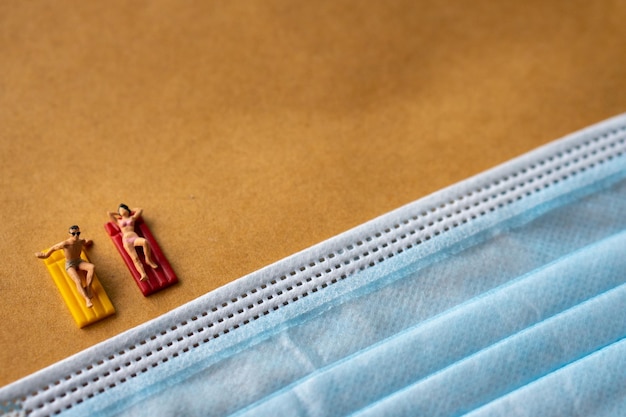 Foto miniaturmenschen spielzeugfigursicherheitsreisekonzept männer und mädchen entspannen sich am strandbett vor blauer gesichtsmaske