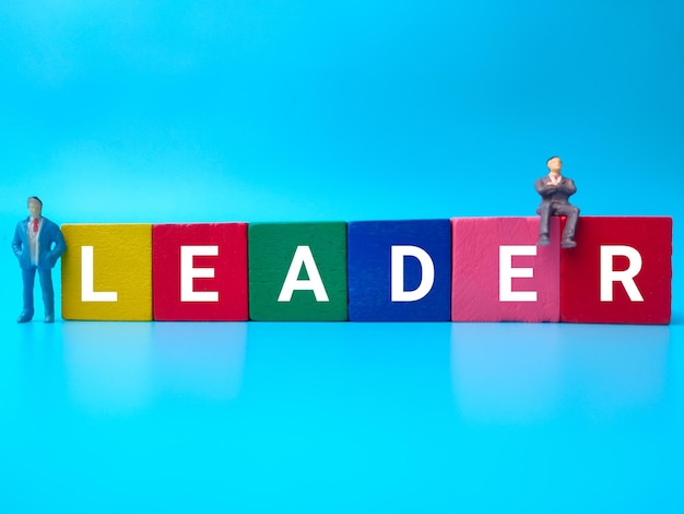 Miniaturmenschen und farbiger Holzwürfel mit dem Wort LEADER auf blauem Hintergrund