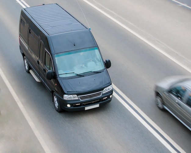 Minibus de carga preto dirigindo na rodovia fora da paisagem de plano médio da cidade