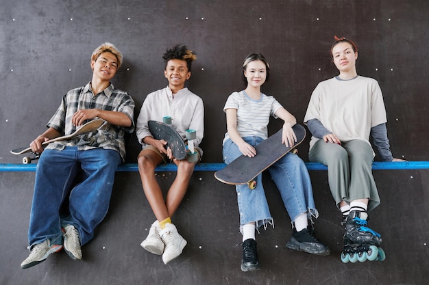 Minimale Aufnahme einer vielfältigen Gruppe von Teenagern, die in die Kamera schauen, während sie beim Skateboarden auf einer Rampe sitzen
