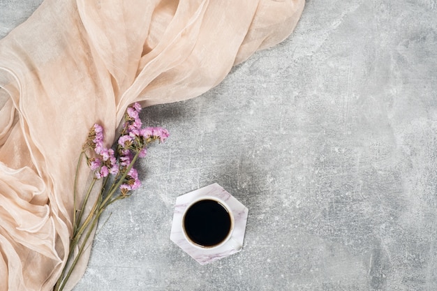 Minimale flache Lagezusammensetzung mit Schal, Kaffeetasse, rosa trockene Blumen auf Betondecke.