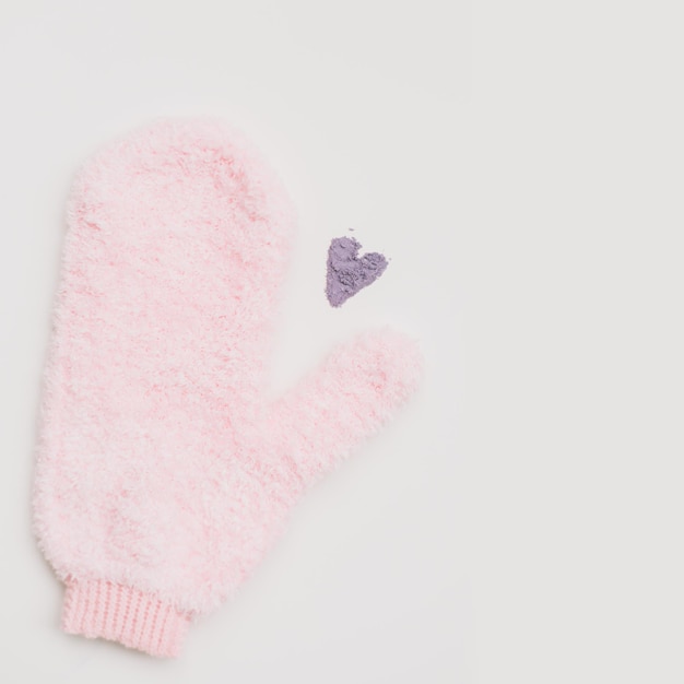 Minimale flache Lay-Komposition aus Massagehandschuh-Waschlappen und einem Herzen aus violettem Puder auf weißem Hintergrund. Konzept von Zero Waste.