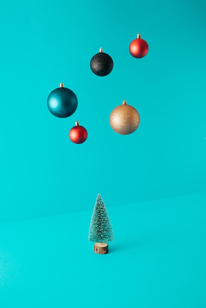 Minimale Komposition mit Weihnachtsbaum und Kugeln, die auf türkisfarbenem Hintergrund schweben