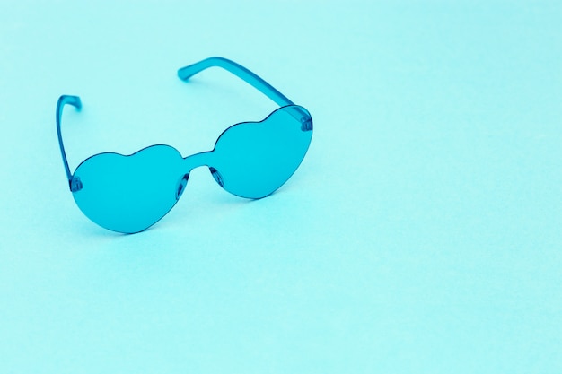 Minimale Modefotografie mit herzförmiger Brille auf Blau. Hellblaue moderne Sonnenbrille. Trendiges Sommerkonzept. Speicherplatz kopieren.