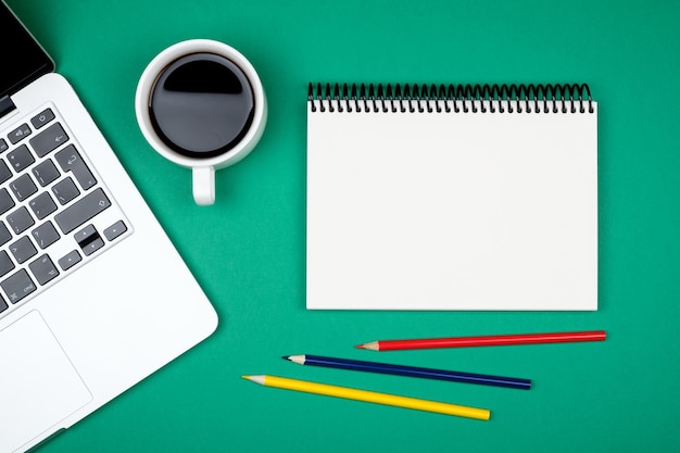 Minimaler Arbeitsplatz mit Laptop und leerem Notizblock auf farbigem Hintergrund, Draufsicht, flache Lage