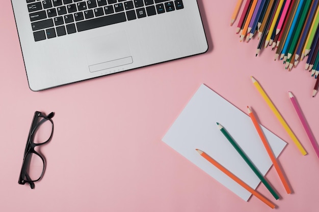 Minimaler Arbeitsplatz mit Laptop und leerem Notizblock auf rosa Hintergrund
