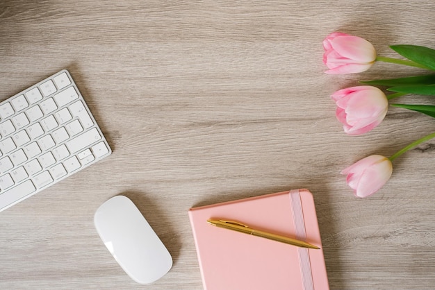 Minimaler Büroschreibtisch mit Tastaturcomputermaus rosa Tulpenblumen auf Holzschreibtisch