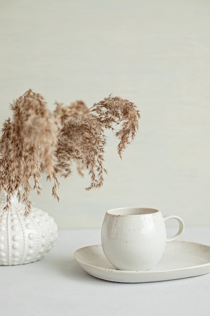 Minimaler Tisch mit Kaffeetasse in Bio-Farbe und Vase mit getrockneten Kräutern