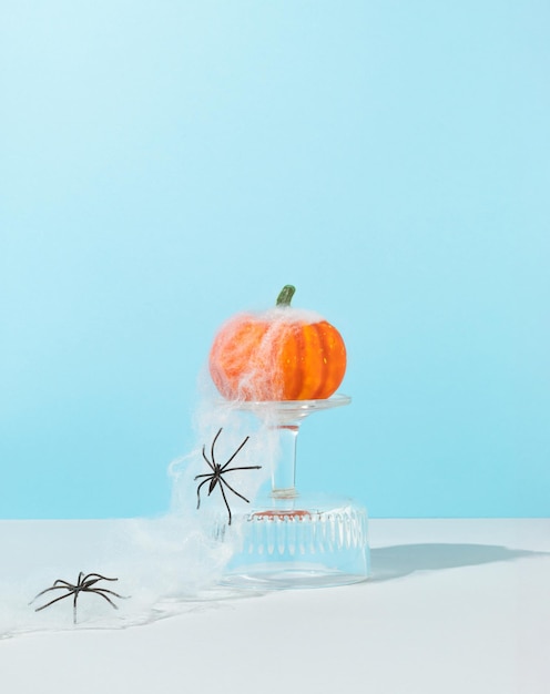 Minimales gruseliges Halloween-Konzept aus Kürbis auf Glaspodium mit Spinnennetz und Spinnen
