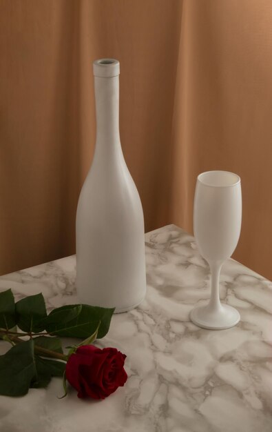 Minimales Konzept im Vintage-Stil mit Weißweinflaschenglas und roter Rosenblüte auf Marmortisch
