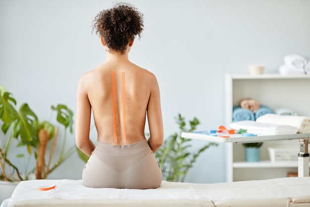 Minimales Porträt einer jungen Frau mit Physio-Tape auf nacktem Rücken im Kopienraum der Reha-Klinik