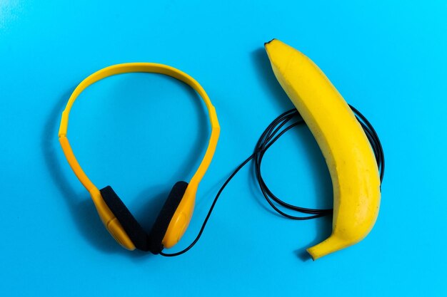 Minimalismo concepto plano laico escucha música Auriculares banana sobre fondo azul Vista superior