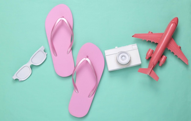 Minimalismus-Reiselayout Flipflops weißes Kameraflugzeug und Sonnenbrille auf mintblauem Hintergrund Draufsicht Flach liegend