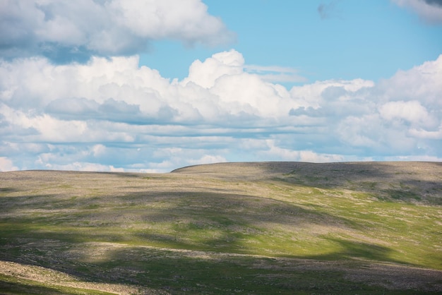 Minimalistische Landschaft mit grüner Bergkette mit Sonnenlicht und Schatten von Wolken bei wechselhaftem Wetter Minimaler Naturhintergrund mit sonnenbeschienenen Bergen und bewölktem Himmel Cumulus-Wolken am blauen Himmel