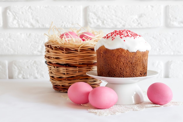 Minimalistische Osterkomposition mit Weidenkorb mit rosa gefärbten Eiern und Osterkuchen auf weißem Hintergrund