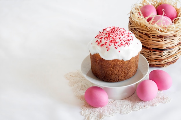 Minimalistische Osterkomposition mit Weidenkorb mit rosa gefärbten Eiern und Osterkuchen auf weißer Oberfläche