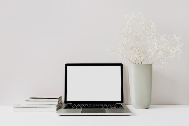 Minimalistischer Arbeitsbereich des Home-Office-Schreibtisches mit Laptop, Blumenstrauß auf Rosa