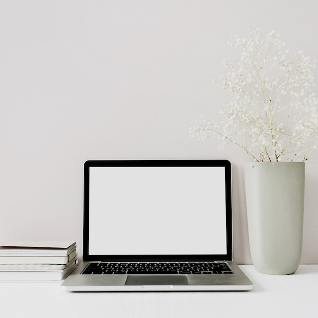 Minimalistischer Arbeitsbereich des Home-Office-Schreibtisches mit Laptop, Blumenstrauß auf Rosa