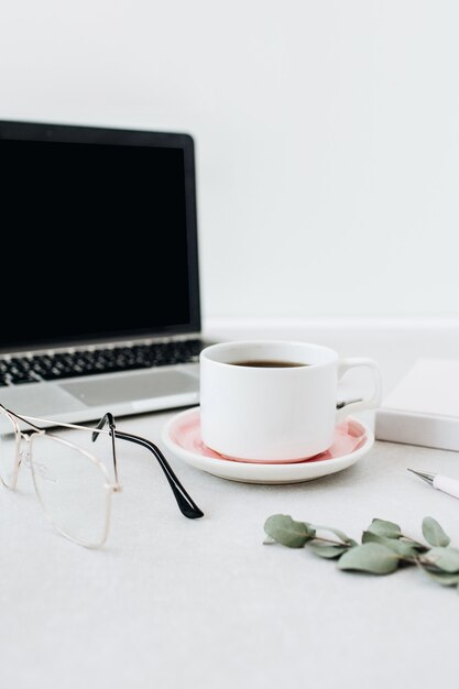 Minimalistischer Arbeitsbereich für den Home-Office-Schreibtisch. Laptop, Kaffee, Gläser, Notizbuch, Eukalyptus