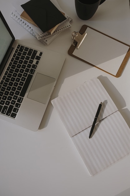 Minimalistischer Home-Office-Schreibtisch-Arbeitsplatz. Laptop auf Tisch mit Kaffeetasse, Papierblatt, Briefpapier gegen weiße Wand