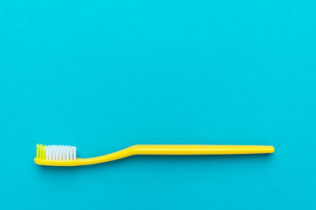 Minimalistisches, flaches Foto einer gelben Zahnbürste auf türkisblauem Hintergrund