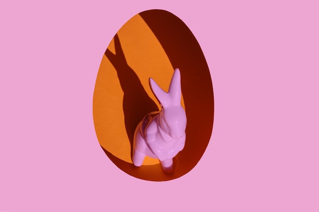 Minimalistisches Osterkonzept, kreatives Layout mit rosa Porzellankaninchen in orangefarbenem Ei mit hartem Sonnenschatten auf leuchtend rosa Hintergrund, Kopierraum