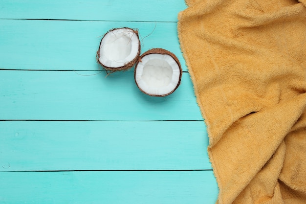 Minimalistisches tropisches Urlaubskonzept. Kokosnusshälften, Handtuch auf einem blauen hölzernen Hintergrund. Draufsicht