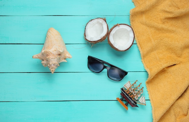 Minimalistisches tropisches Urlaubskonzept. Kokosnusshälften, Strandzubehör, Handtuch auf einem blauen hölzernen Hintergrund. Draufsicht