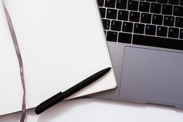 Mínimo espacio de trabajo. Un cuaderno en blanco con un bolígrafo negro se encuentra en el teclado de una computadora portátil