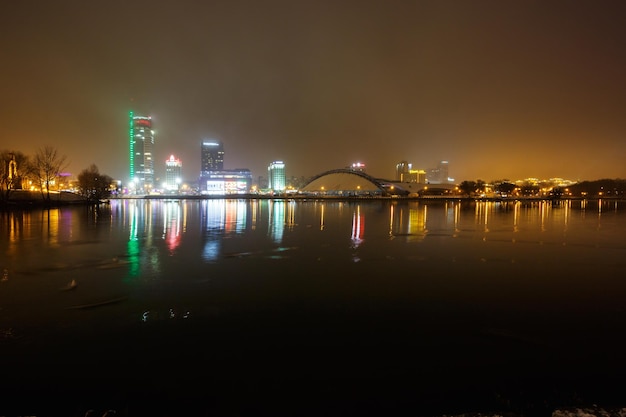 MINSK BELARUS 8. DEZEMBER 2017 Lichter der Nachtstadt Leichter Wolkenkratzer spiegelt sich im Seewasser mit Nebel wider