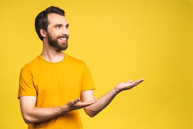 ¡Mira allá! Hombre guapo joven feliz en casual apuntando hacia afuera y sonriendo mientras está de pie aislado sobre fondo amarillo.