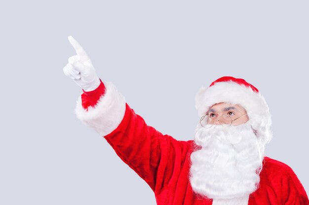 ¡Mira allá! Santa Claus tradicional apuntando hacia afuera mientras está de pie contra el fondo gris