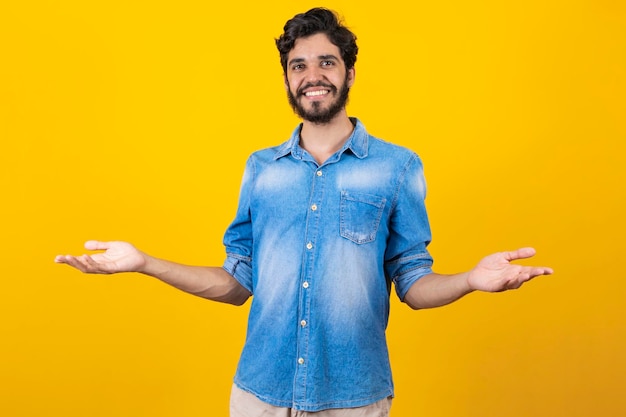 Mira allí Feliz joven apuesto con camisa de mezclilla apuntando hacia otro lado y sonriendo mientras está de pie contra el fondo amarillo