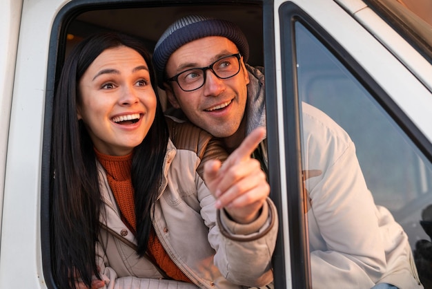 Mira allí. Pareja positiva enamorada señalando con el dedo mientras se sienta en el auto durante un picnic en el bosque y sonriendo frente a la cámara