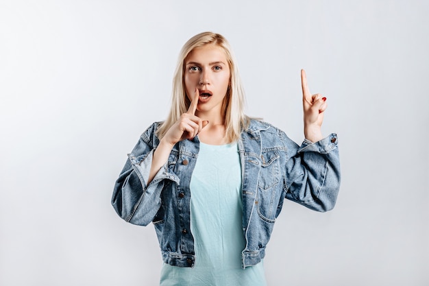 Mira aquí. Joven y bella mujer rubia apunta sus dedos a la parte superior piensa y toma una decisión. La mujer pensó en la elección. Lugar para publicidad.