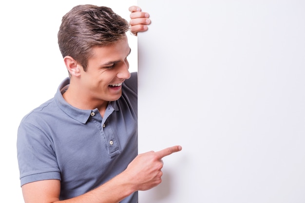 ¡Mira eso! Feliz joven apuntando copia espacio y sonriendo mientras está de pie contra el fondo blanco.