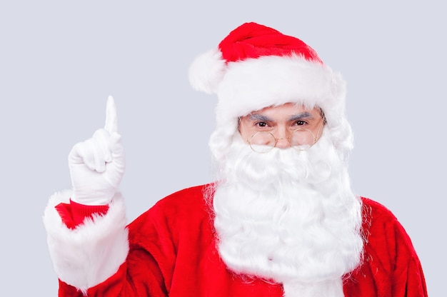 ¡Mira eso! Papá Noel tradicional apuntando hacia arriba mientras está de pie contra el fondo gris