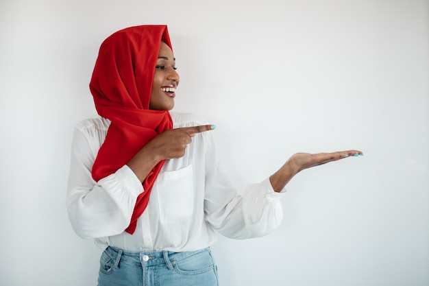Mira esta feliz mujer musulmana afroamericana con hiyab señalando algo en su maqueta de palma vacía