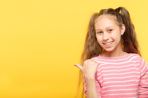 Mira a la izquierda. niña sonriente apuntando con su dedo índice a un objeto virtual o texto