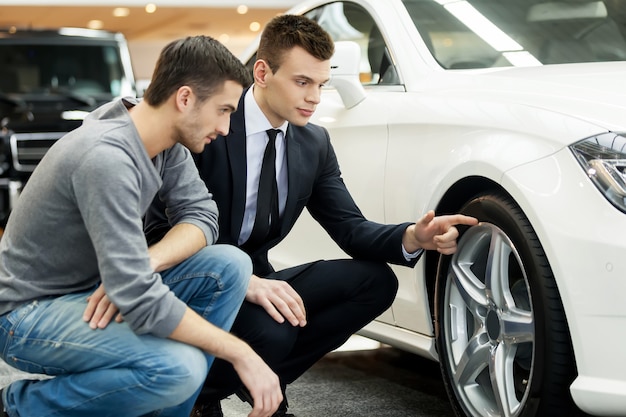 ¡Mira estos neumáticos! Vendedor de coches joven que muestra las ventajas del coche al cliente.