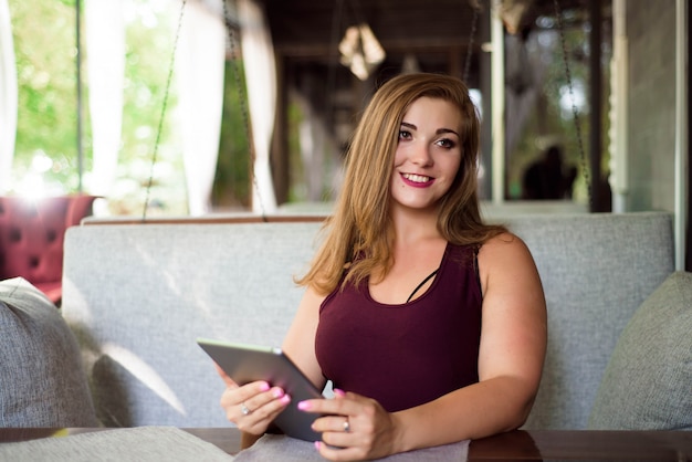 Mirada cotidiana. Modelo de talla grande. Hermosa mujer joven con una tableta en un restaurante.