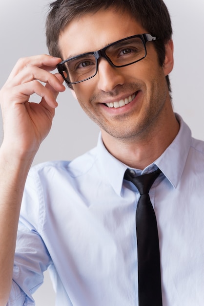 Mirada experta. Retrato de joven guapo en camisa y corbata ajustando sus anteojos y sonriendo