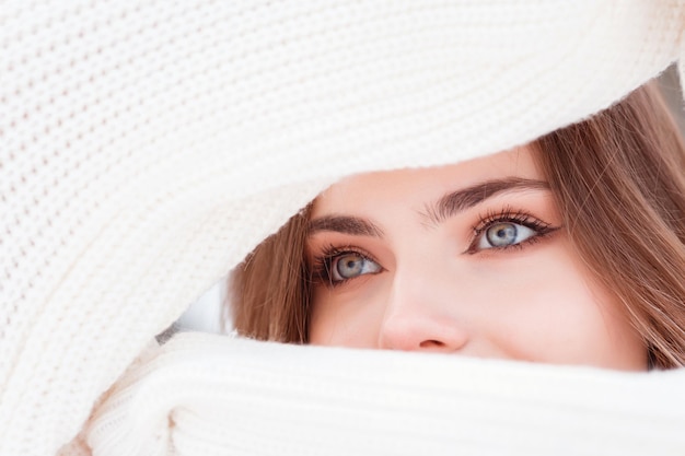 Mirada expresiva de hermosos ojos de mujer a través de mangas de suéter de punto blanco, temporada de invierno.