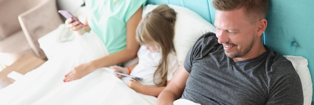 Mirada familiar en la mañana del teléfono inteligente en la cama con dispositivos para matar el tiempo