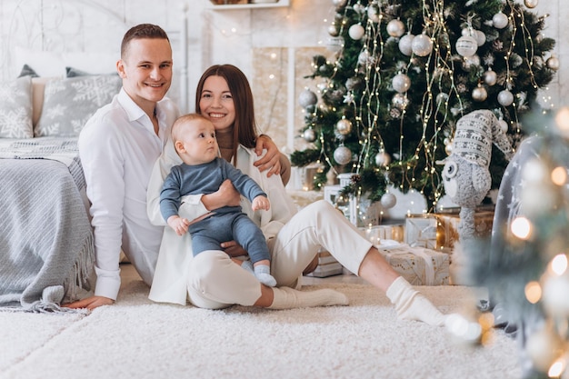 Mirada sorprendida. Encantadora familia se sienta cerca del árbol de Navidad con cajas de regalo en la noche de invierno