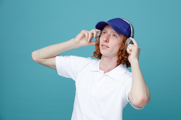 Mirando al lado joven apuesto con gorra usando auriculares aislados en fondo azul