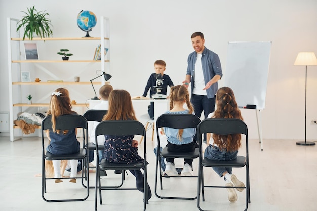 Mirando al niño con el microscopio que está en la mesa Grupo de niños estudiantes en clase en la escuela con el maestro